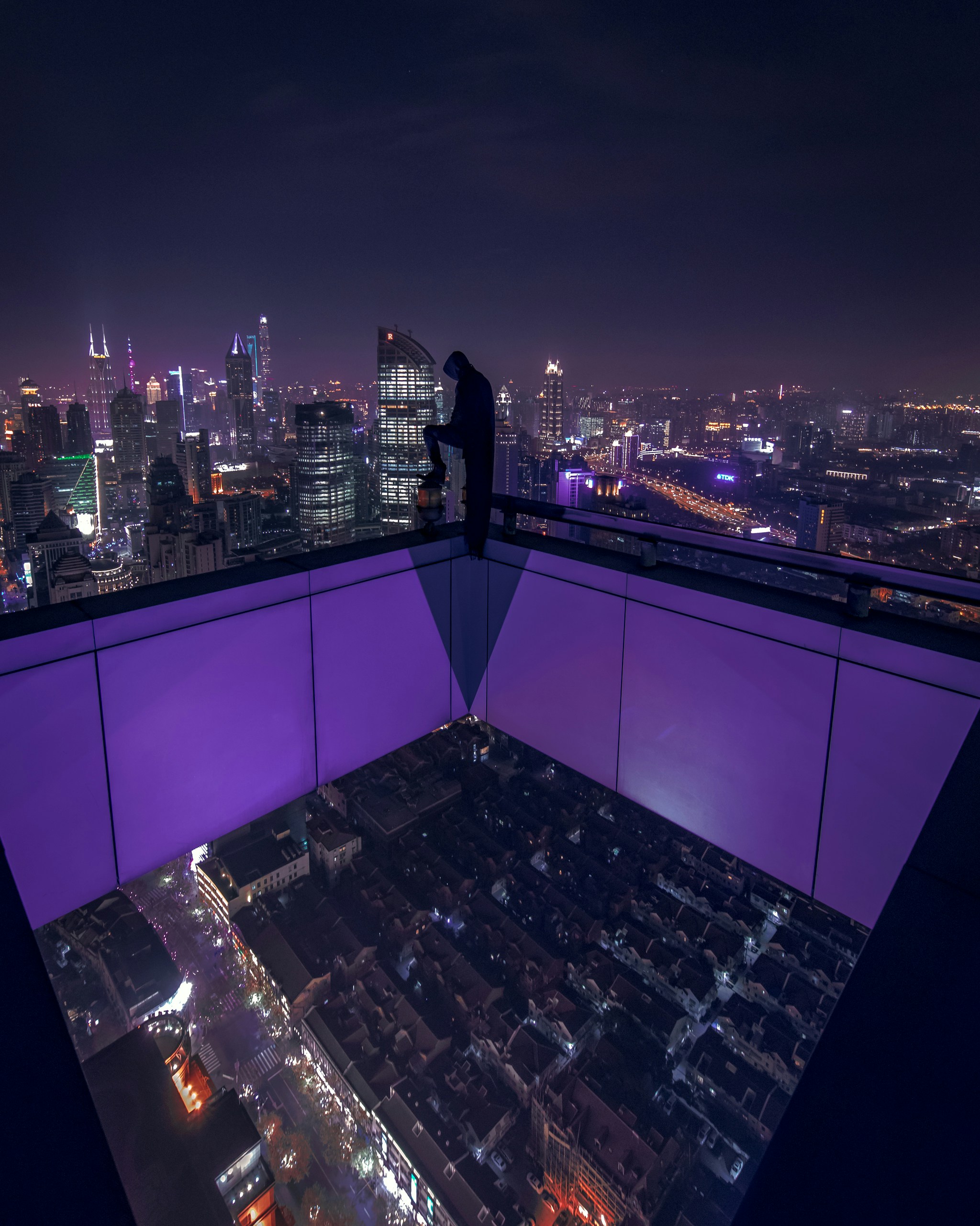 Person standing on a purply lit edge of a tall building